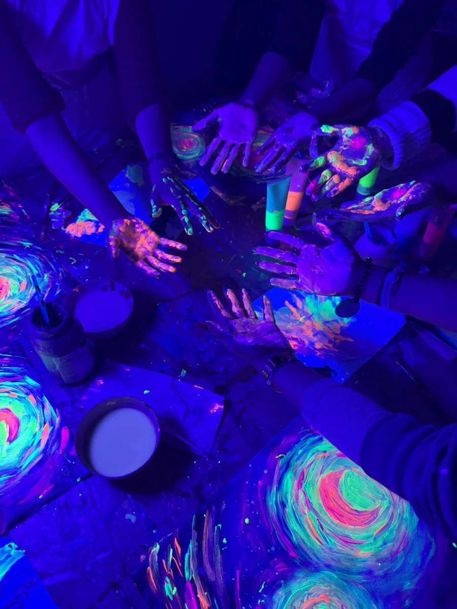 Manos cubiertas de pintura neón sobre cuadros de espirales fluorescentes